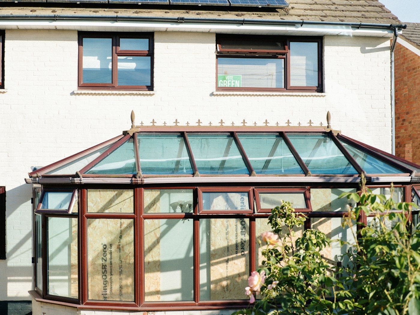 A conservatory with a glazed roof attached to the back of a white house.